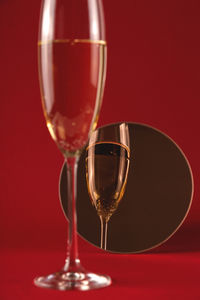 Glass of champagne with reflection in a small round mirror on a red background. 