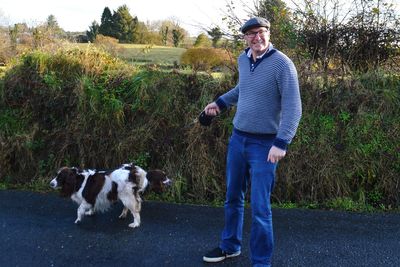 Full length of smiling man with dog standing on road by plants