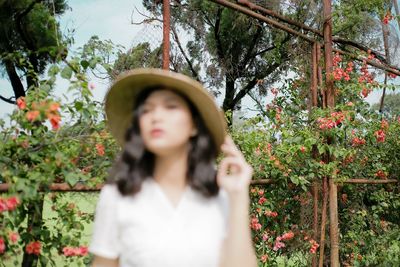 Portrait of young woman standing by flowering plants