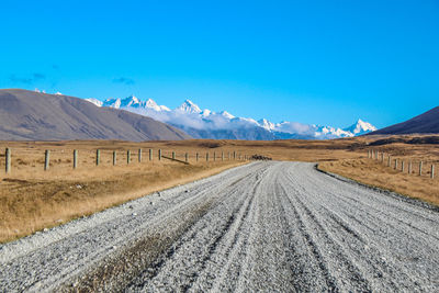 Scenic view of empty road by mountains against blue sky