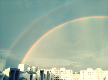 Rainbow over city against cloudy sky