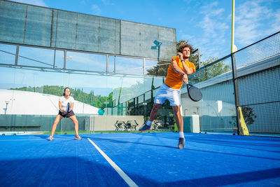 Full length of young man playing tennis with friend in court