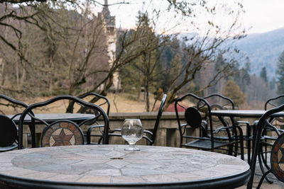 Empty chairs and tables by trees against forest, mountain and sky