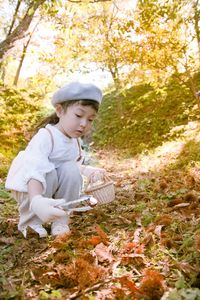 Cute girl with basket crouching on field during autumn