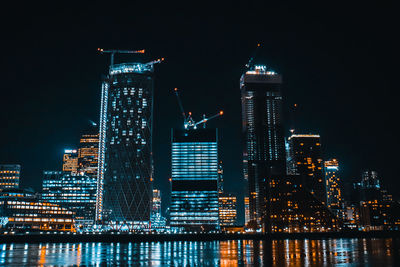 Illuminated buildings reflecting on river against sky at night