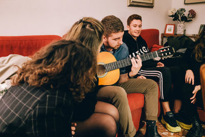 Full length of man playing guitar on sofa