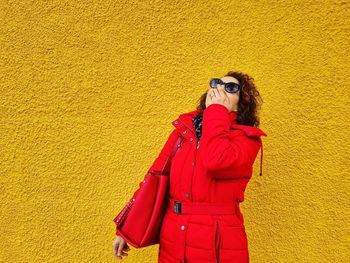 Woman with red jacket in front of a yellow wall laughs and covers his mouth with his hand