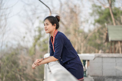 Side view of young woman standing against trees