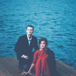 Beautiful couple of lovers. man in a suit and woman in a red dress sitting on the pier by the lake.