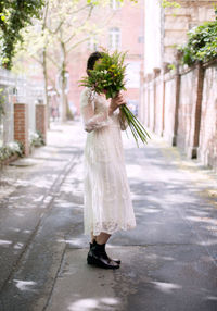 Side view of bride holding bouquet while standing on street
