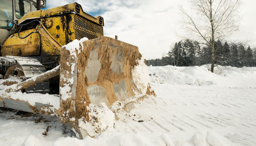 Yellow crawler tractor bulldozer with a bucket works in winter clearing the road from snow. 