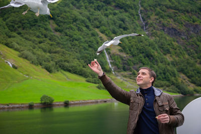 Man feeding bird by lake against mountain