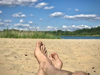 Low section of person relaxing on beach against sky