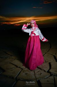 Portrait of young woman standing on field against sky at night