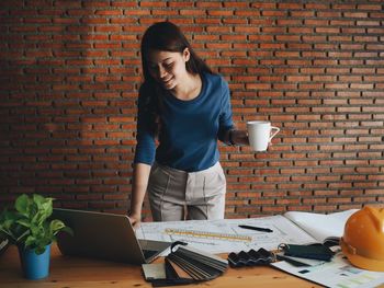 Woman looking at camera while standing against brick wall