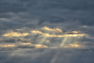 Low angle view of sunlight streaming through clouds