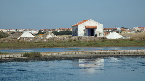 Buildings by lake against clear blue sky