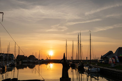 Sailboats moored at harbor during sunset