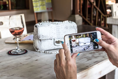 Midsection of person photographing with mobile phone on table