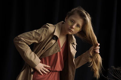 Portrait of young woman standing against black background