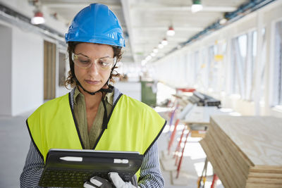 Confident female architect in reflective clothing using digital tablet at construction site