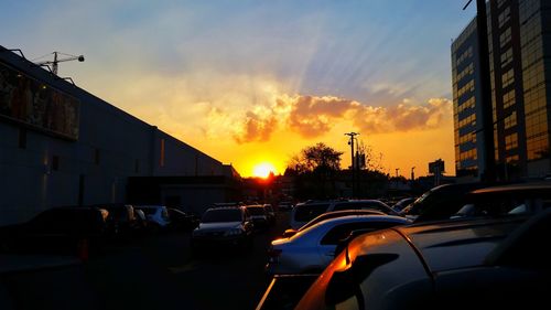 Cars on road in city against sunset sky