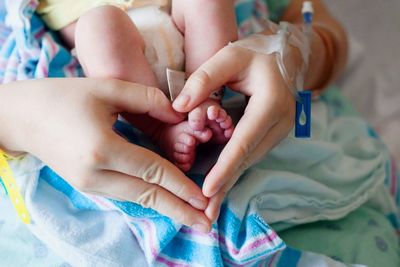 Midsection of mother making heart shape with hands by newborn baby feet in hospital