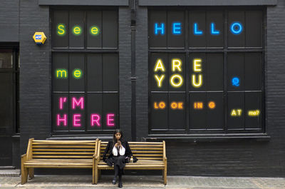 Full length of woman sitting on bench against illuminated wall