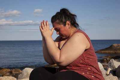 Woman sitting on rock at beach against sky