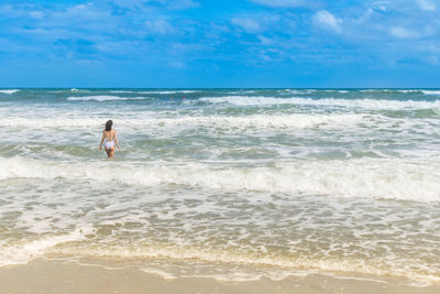 Rear view of woman in bikini at beach against sky