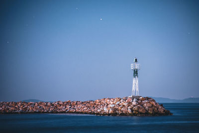 Lighthouse by sea and buildings against clear blue sky