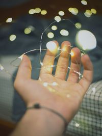 Cropped hand holding string light against bed at home