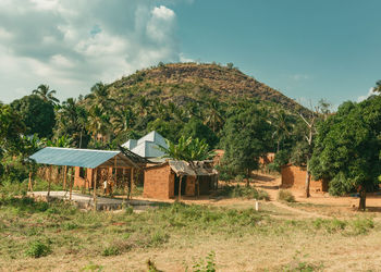 House by trees on field against sky