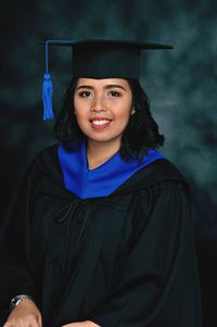 Portrait of smiling young woman in graduation gown against colored background