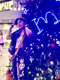 Young woman looking at illuminated christmas tree at night