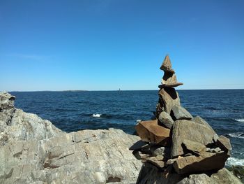Stack of rocks by sea against blue sky