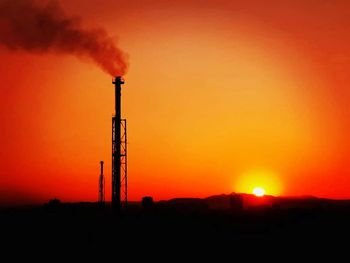 Silhouette of factory against orange sky