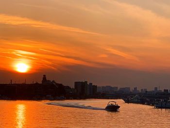 Sea by buildings against sky during sunset