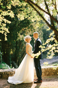 Rear view of couple holding bouquet against trees