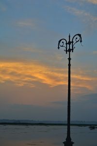 Silhouette wooden post by sea against sky during sunset