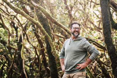 Smiling man looking away while standing against trees