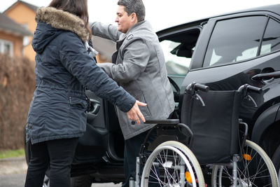 A woman helps aphysical disabled person to get into the car.