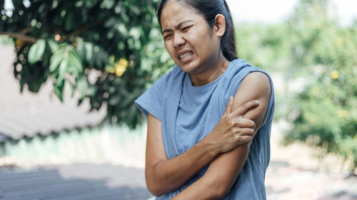 Woman touching shoulder in pain against trees