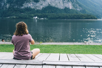 Rear view of man sitting on wooden bench near lake