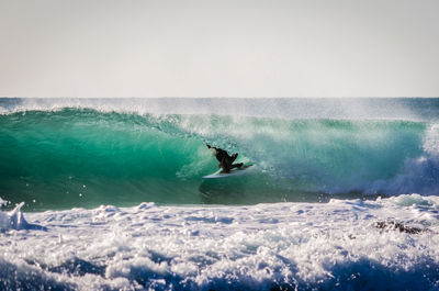 Surfer surfing on sea waves against clear sky