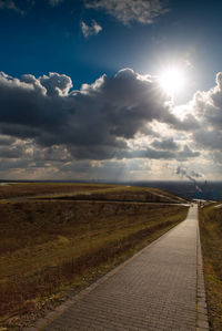 Empty road amidst field against sky