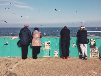 Rear view of people standing at observation point by sea against sky