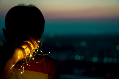 Close-up of mid adult man holding illuminated string lights against sky during sunset