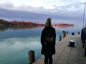 Rear view of man standing by lake against sky