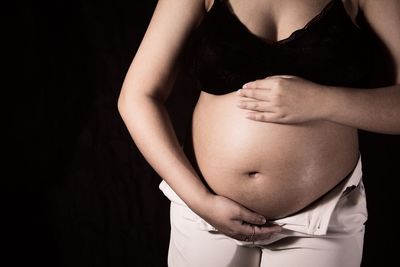 Midsection of woman touching hair against black background